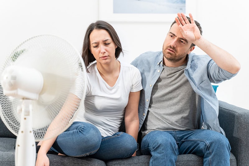 5 Reasons Why Regular HVAC Maintenance is Essential for Homeowners. A couple sitting in their hot house in front of a fan.
