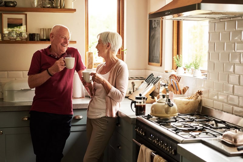 Cold Climate Heat Pumps Are HVAC Game Changers. Photo of an elderly couple enjoying a hot beverage together in their kitchen.