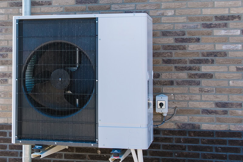 an air-source heat pump mounted against a brick wall.