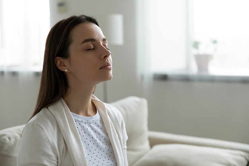 Why Do I Need a Humidifier? A woman sitting on her couch breathing in clean air.